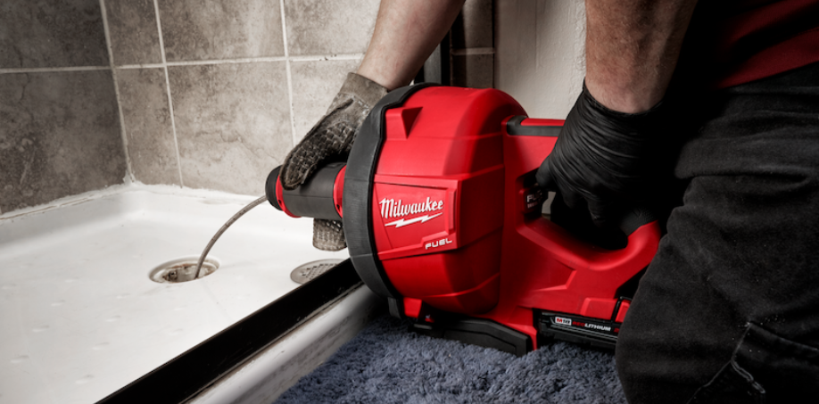 Someone using the Milwaukee M18 Drain Snake to clean a shower drain