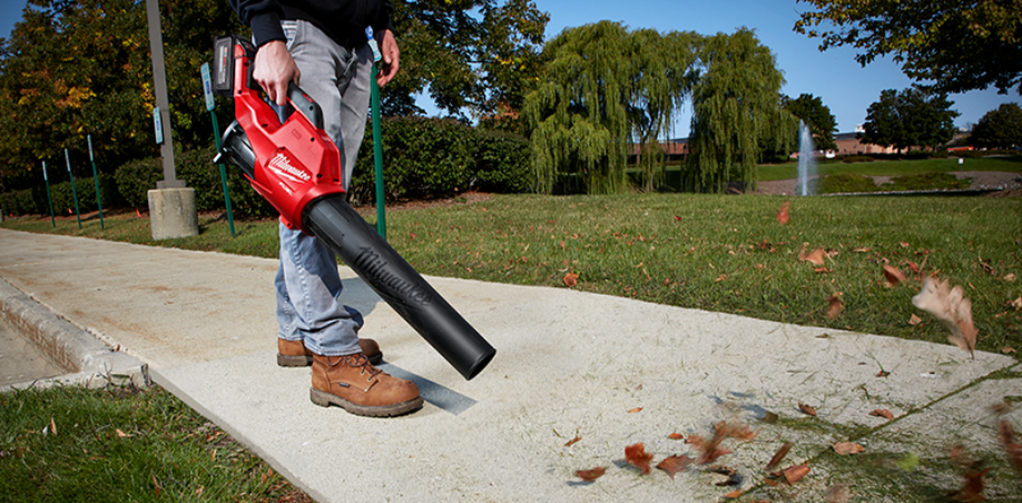 A person using a Milwaukee Blower to blow debris off a sidewalk