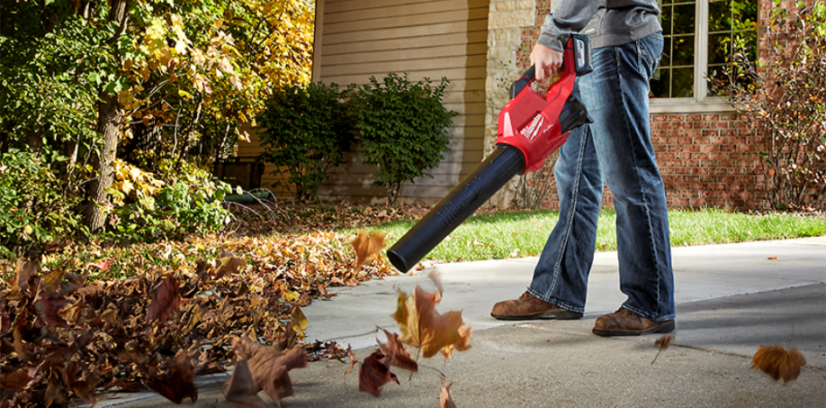 A man using a Milwaukee Leaf Blower to blow leafs off a driveway