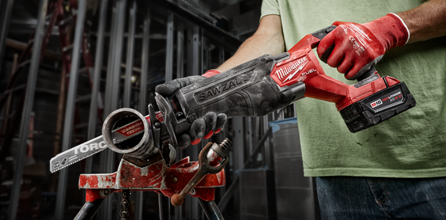 A construction worker using a Milwaukee M18 Sawzall to cut through a piece of metal pipe.