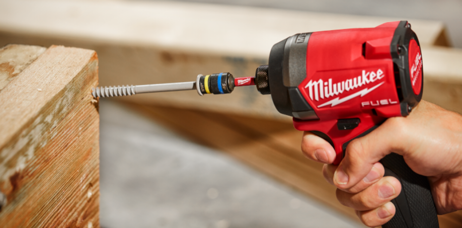 Construction worker driving a screw into a piece of wood with an Milwaukee M18 Imact Driver