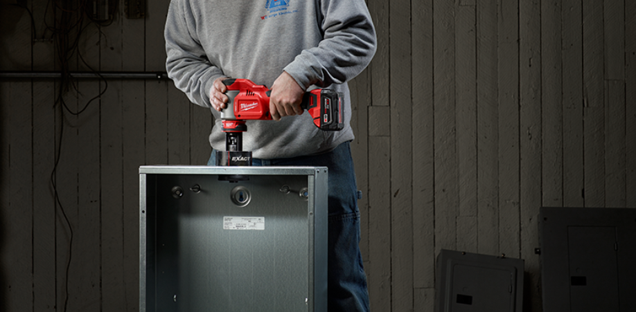 Someone using a Milwaukee M18 Knockout tool to make a hole in a electrical panel