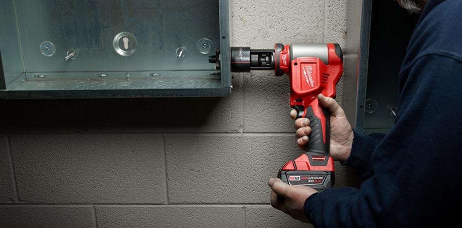 A Milwaukee M18 knockout tool being used to make a hole in a electrical box