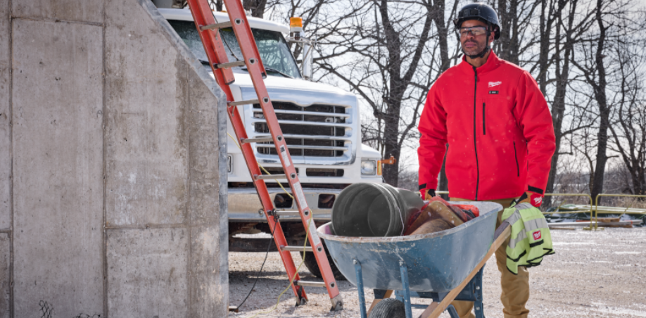 Man pushing a wheel barrow wearing a red Milwaukee M12 Heated Jacket