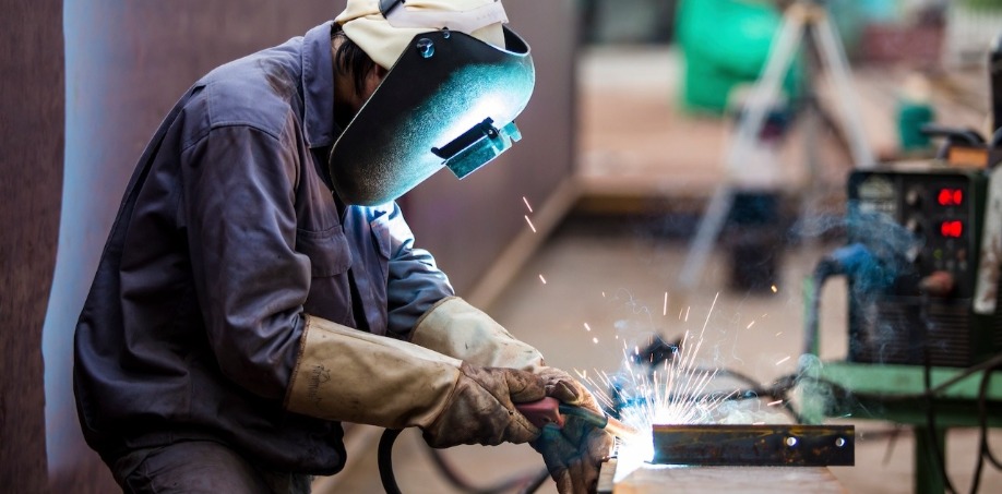 A worker welding steel wearing a welding jacket, a welding helmet and welding gloves