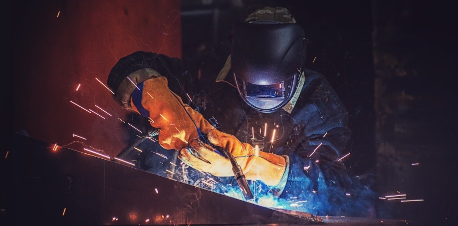 Someone welding steel together wearing a welding helmet and welding gloves